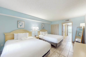 A hotel room with two beds, a nightstand, a lamp, and a door leading to another room. - Camelot by the Sea 1203 (Myrtle Beach)