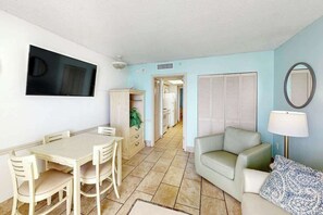 Ein Zimmer mit Esstisch, Stühlen, einer Couch, einer Lampe und einem an der Wand befestigten Fernseher.