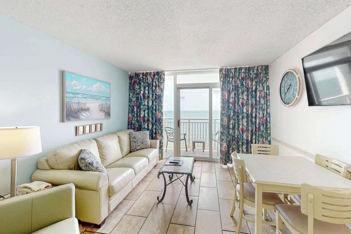 Ein Zimmer mit einer Couch, einem Tisch und Blick auf das Meer durch eine Glasdoor.