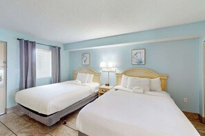 A hotel room with two beds, a window with curtains, bedside lamps, and framed artwork on the wall. - Camelot by the Sea 1203 (Myrtle Beach)
