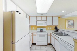 A compact kitchen with white cabinets, a microwave, a stove, and a sink. - Camelot by the Sea 1109 (Myrtle Beach)
