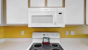 Una cucina con un forno a microonde bianco sopra un piano cottura a quattro fuochi, una parete gialla e un bancone bianco.