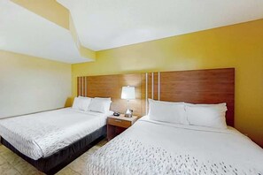 A hotel room with two beds, a wooden headboard, a bedside table with a lamp, and a plain wall. - Camelot by the Sea 1109 (Myrtle Beach)