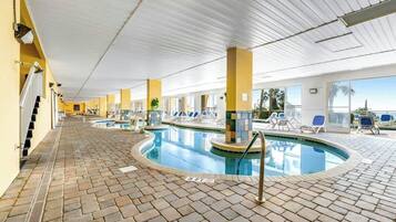 An indoor swimming pool with lounge chairs and a view of the ocean.