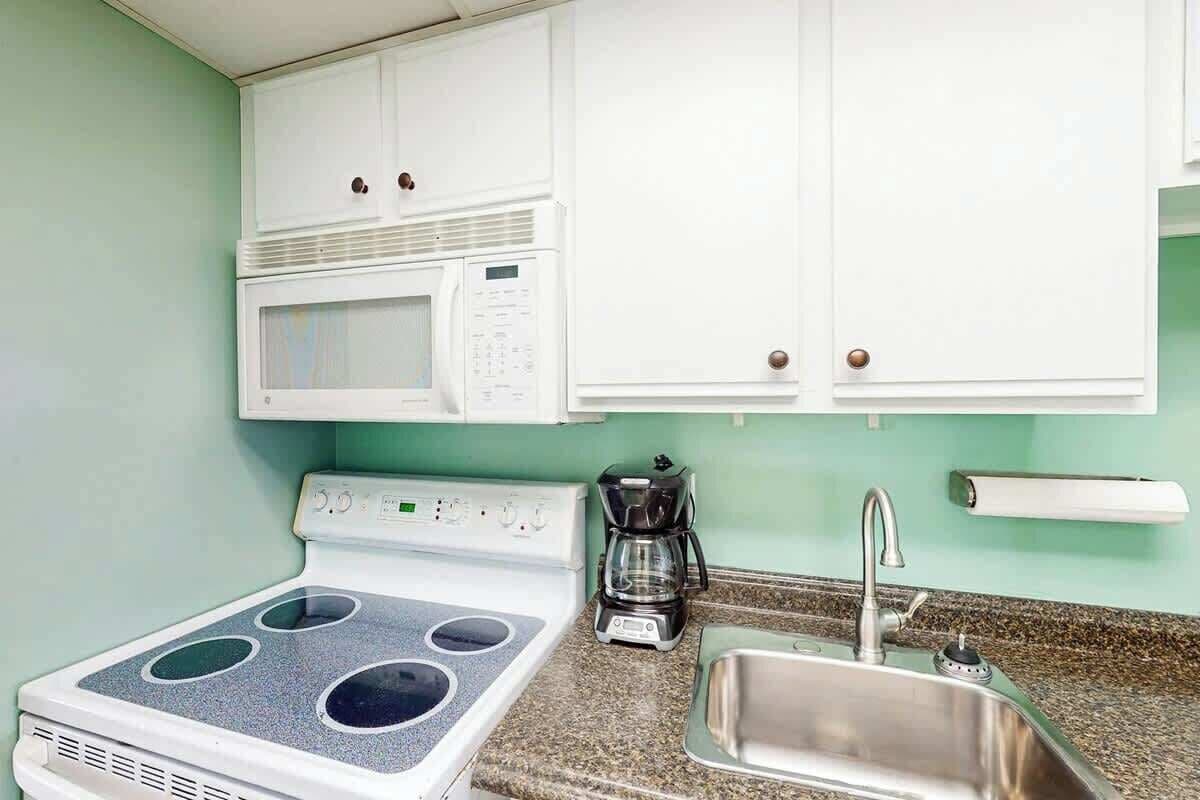 A kitchen with white cabinets, a stove, a microwave, a coffee maker, and a sink.
