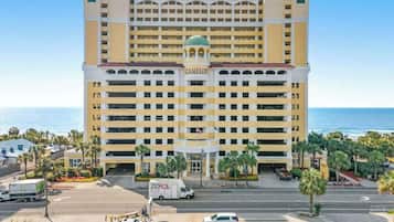 A multi-story hotel with a prominent entrance, a parking area, and a view of the ocean.