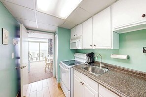 A kitchen with white cabinets, a stove, a microwave, and a sink. - Camelot by the Sea 1214 (Myrtle Beach)