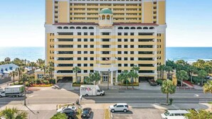 A multi-story hotel with a prominent entrance, a parking area, and a view of the ocean. - Camelot by the Sea 1207 (Myrtle Beach)
