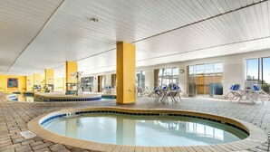 An indoor swimming pool area with a tiled floor, lounge chairs, and a pool with a tiled edge. - Camelot by the Sea 1207 (Myrtle Beach)