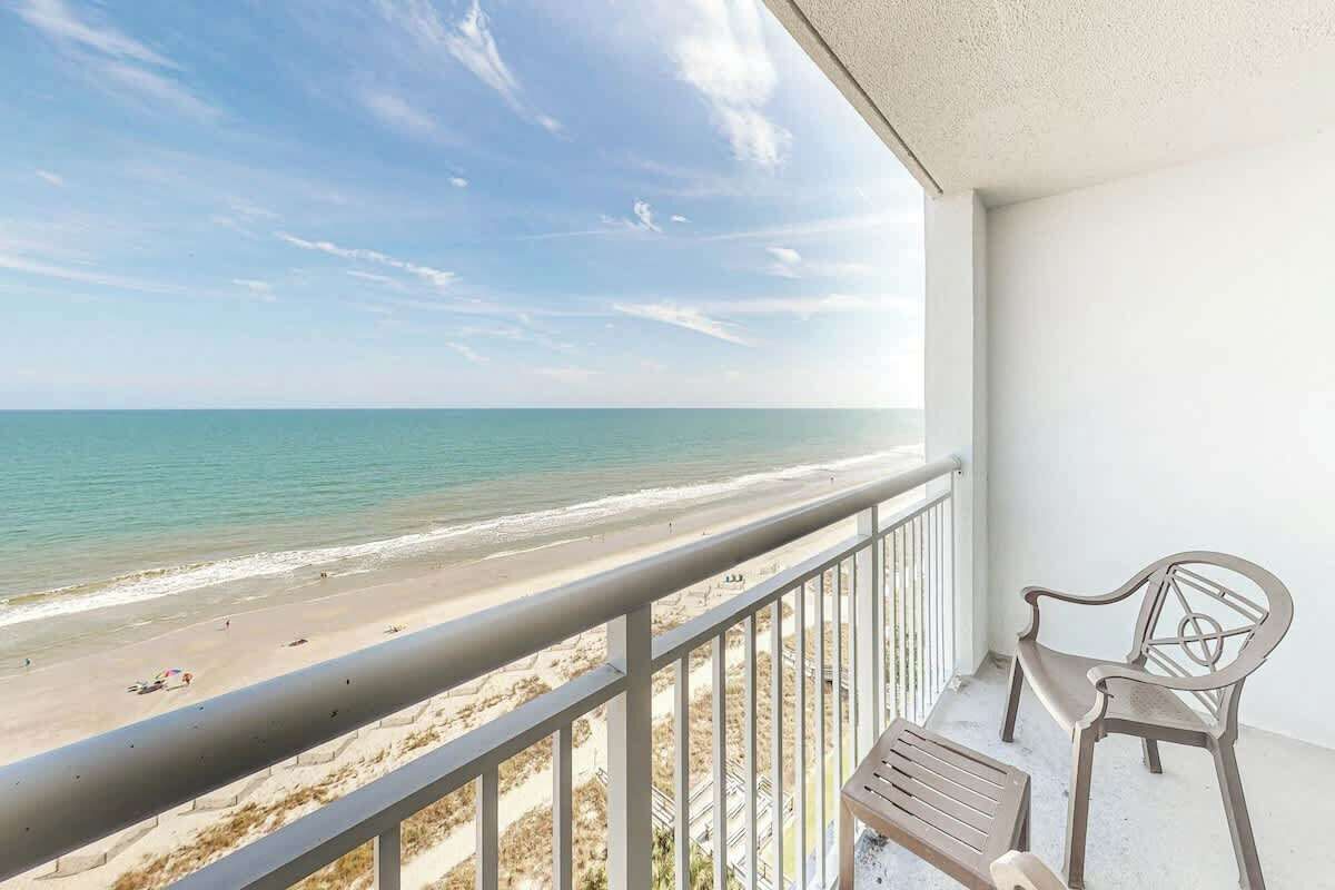 Un balcon avec vue sur une plage et l’océan, une chaise et une petite table.