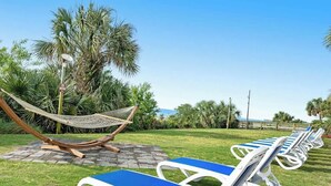 A row of sun loungers with blue cushions, a hammock, and palm trees in the background. - Camelot by the Sea 1405 (Myrtle Beach)