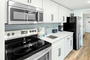 A modern kitchen with stainless steel appliances, white cabinetry, and a tiled backsplash. - Camelot by the Sea 1405 (Myrtle Beach)
