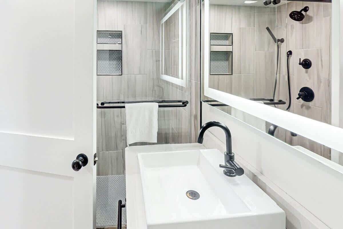 Een moderne badkamer met een witte wastafel, een handdoekhouder, een spiegel en een douche met een handdouche.