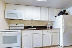 Una cocina con armarios blancos, un microondas, una estufa, un refrigerador y una cafetera sobre la encimera.