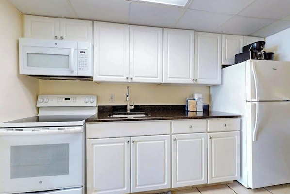 A kitchen with white cabinets, a microwave, a stove, a refrigerator, and a coffee maker on the countertop. - Camelot by the Sea 1216 (Myrtle Beach)