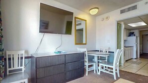 Ein kompakter Wohnbereich mit Küchenzeile, einem Essbereich mit Tisch und Stühlen, einem an der Wand befestigten Flachbildfernseher und einem Spiegel.