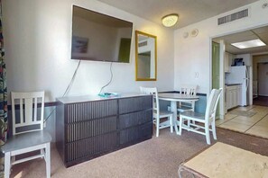 A compact living space with a kitchenette, a dining area with a table and chairs, a flat-screen TV mounted on the wall, and a mirror. - Camelot by the Sea 1216 (Myrtle Beach)