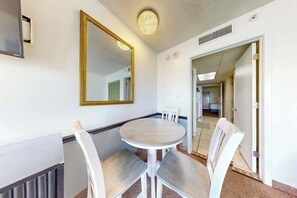 A hotel room with a round table and four chairs, a large mirror, and a door leading to another room. - Camelot by the Sea 1216 (Myrtle Beach)
