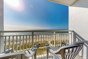 A balcony with a view of a beach, featuring two chairs and a table. - Camelot by the Sea 1216 (Myrtle Beach)