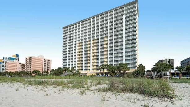 Ein Hotel direkt am Strand mit Hochhausarchitektur, Sandstrand und Palmen.