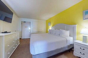 Habitació d'hotel amb un llit, una petita taula de nit, un calaixera i una televisió penjada a la paret, i una porta que dóna a una altra habitació.