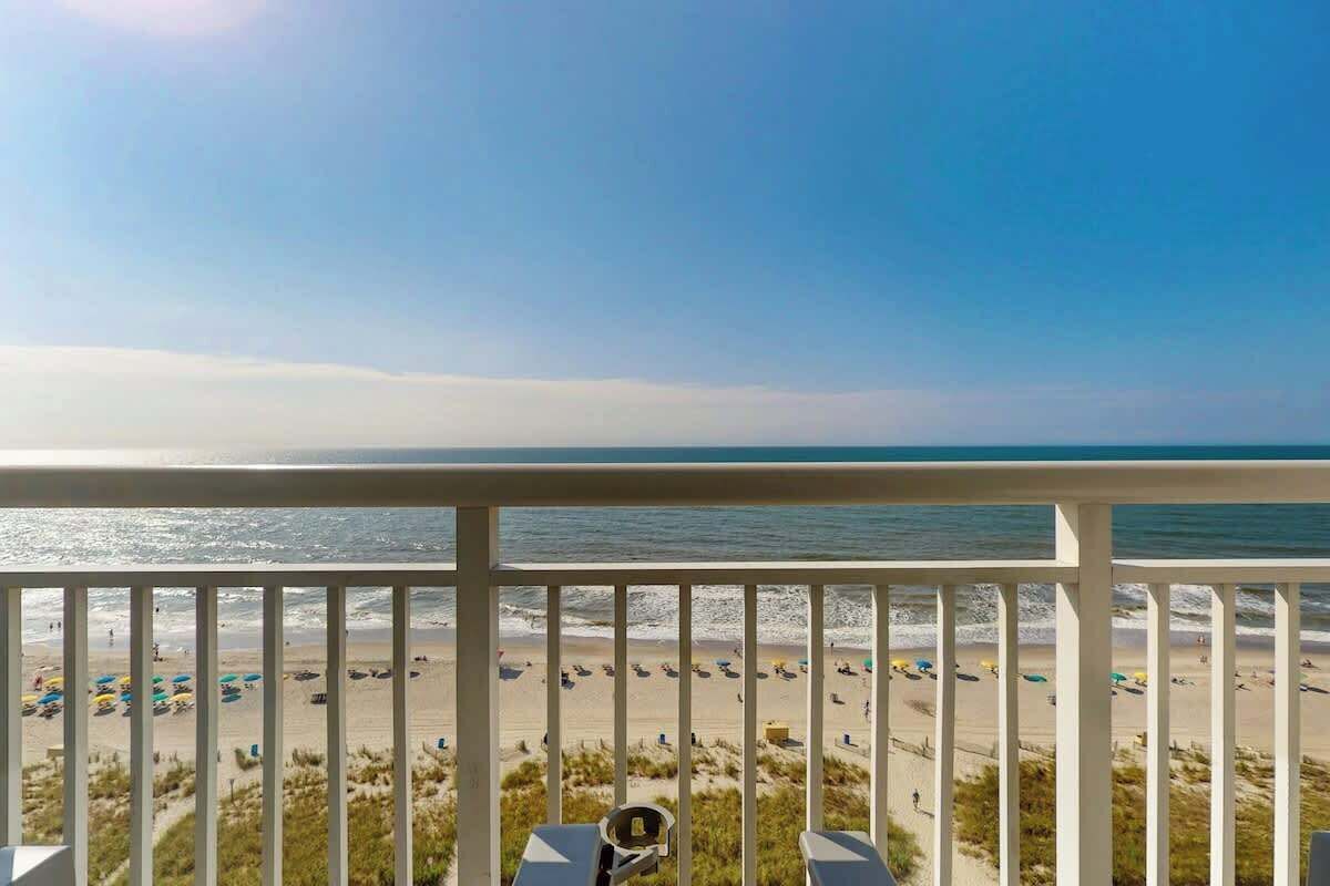 A balcony with a view of a beach, including the ocean and sandy shore.