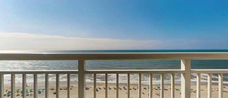A balcony with a view of a beach, including the ocean and sandy shore.