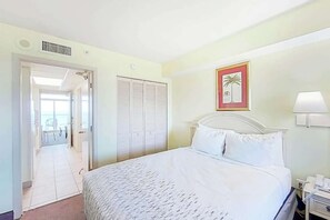 Ein Hotelzimmer mit einem Bett, einem Nachttisch, einer Lampe, einer Tür, die auf einen Balkon führt, und einem gerahmten Bild an der Wand.