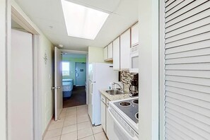 Un couloir étroit mène à une cuisine équipée d’une fenêtre, d’un réfrigérateur et d’une cuisinière.