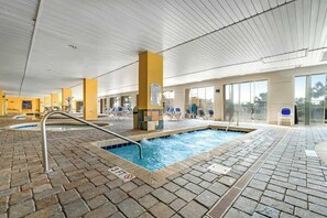 An indoor swimming pool with a brick floor, lounge chairs, and a clear view of the outside. - Camelot by the Sea 1512 (Myrtle Beach)