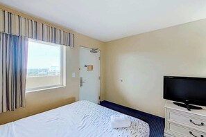 Een hotelkamer met een bed, een televisie op een dressoir en een raam met gordijnen.