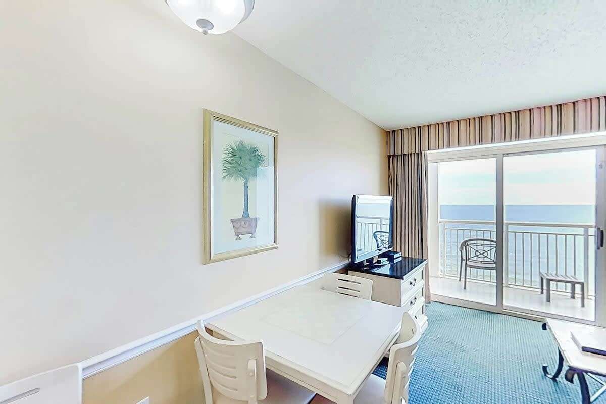 A hotel room with a balcony, a desk, a chair, a television, and a framed picture on the wall.