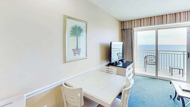 Ein Hotelzimmer mit Balkon, Schreibtisch, Stuhl, Fernseher und einem gerahmten Bild an der Wand.