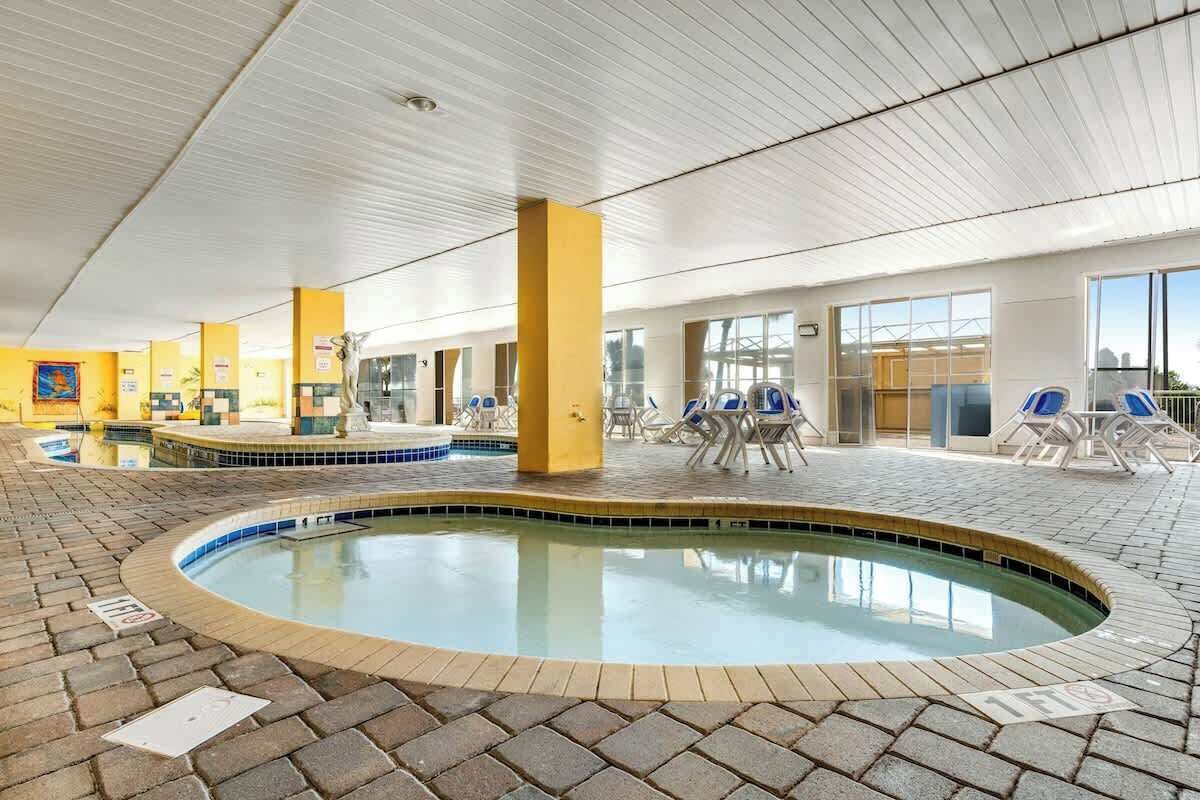 An indoor swimming pool with lounge chairs and a tiled floor.