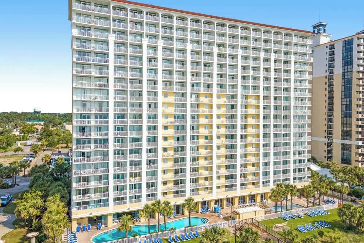A multi-story hotel with a pool area, outdoor seating, and a view of the surrounding landscape.