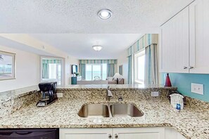 A kitchen with granite countertops, a double sink, and a coffee maker. - Camelot by the Sea 1601 (Myrtle Beach)