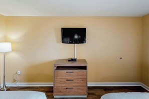 A room with a television mounted on the wall, a wooden nightstand with drawers, and a lamp. - Camelot by the Sea 1514 (Myrtle Beach)