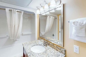 Ein Badezimmer mit Marmorwaschtisch, einem großen Spiegel und einer Dusche mit Glastür.