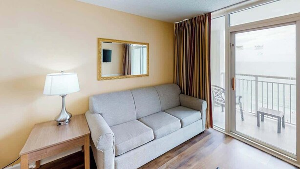 Ein Hotelzimmer mit einer Couch, einem Nachttisch mit Lampe, einem Spiegel und einer Schiebetür zu einem Außenbereich.