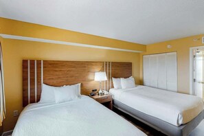 Ein Hotelzimmer mit zwei Betten, einem hölzernen Kopfteil, einem Nachttisch mit Lampe und einem Schrank mit weißen Läden.