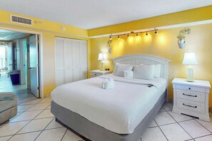 A hotel room with a bed, two bedside tables, a chair, and a door leading to another room. - Camelot by the Sea 1804 (Myrtle Beach)
