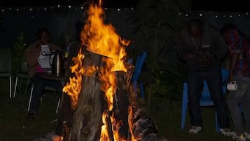 A campfire with logs arranged in a circle, surrounded by chairs and people.