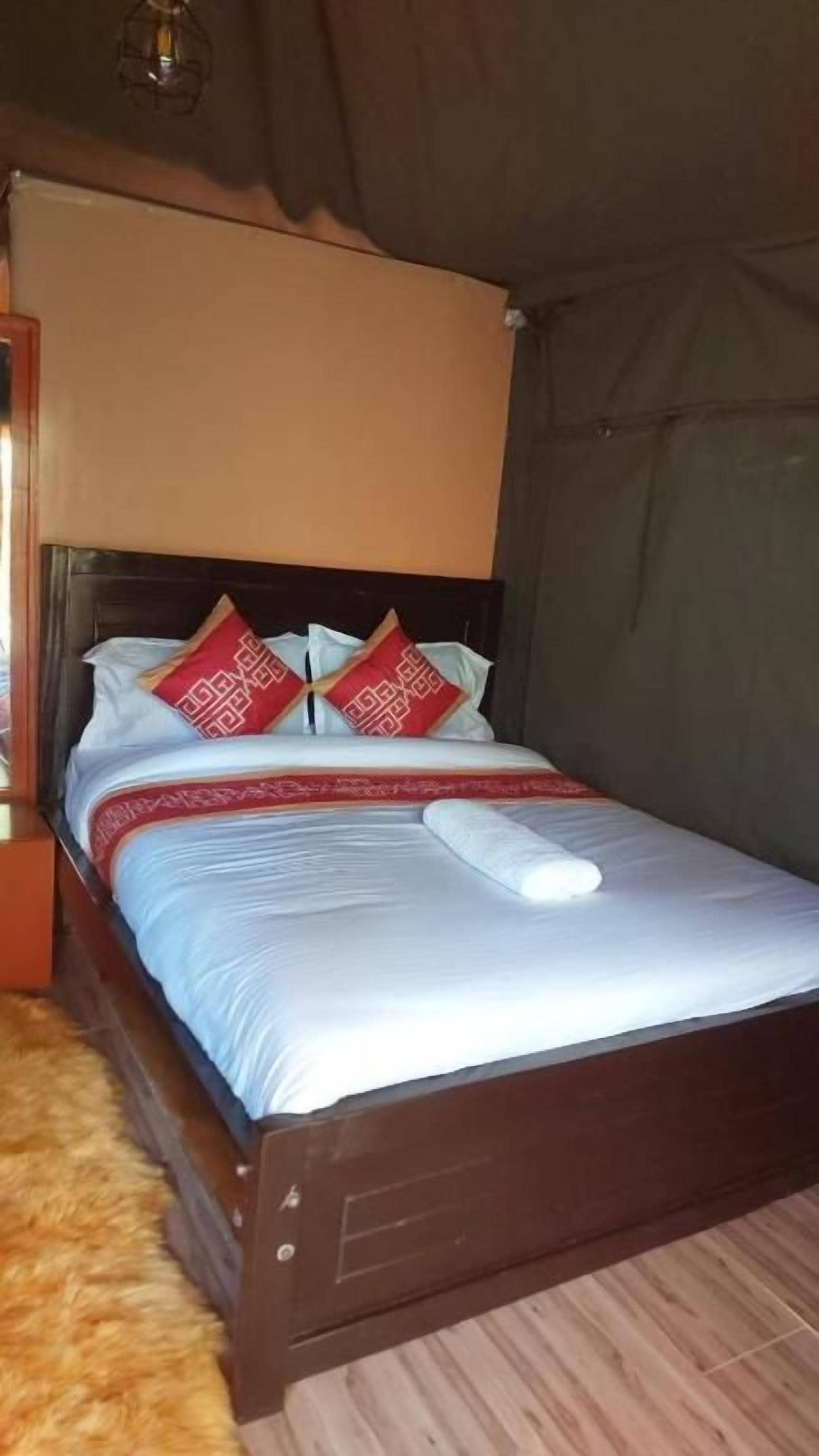 A single bed with a wooden frame, a white mattress, and red patterned pillows.