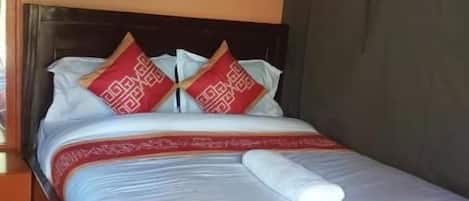 A single bed with a wooden frame, a white mattress, and red patterned pillows.