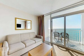 A hotel room with a sofa, a coffee table, a mirror, and a balcony with a view of the sea. - Camelot by the Sea 1607 (Myrtle Beach)