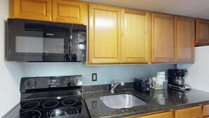 A kitchen with wooden cabinets, a black microwave, a stove, and a sink. - Camelot by the Sea 1603 (Myrtle Beach)