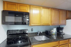 A kitchen with wooden cabinets, a black microwave, a stove, and a sink. - Camelot by the Sea 1603 (Myrtle Beach)