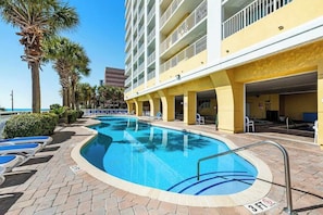 A swimming pool with lounge chairs, a building with balconies, and palm trees. - Camelot by the Sea 1603 (Myrtle Beach)
