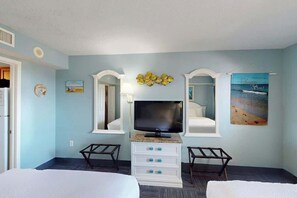 Une chambre d’hôtel avec un lit, une télévision, une commode et un tableau représentant une plage.