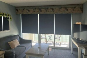 Uma sala de estar com sofá, mesa de centro, televisão e varanda com vista.